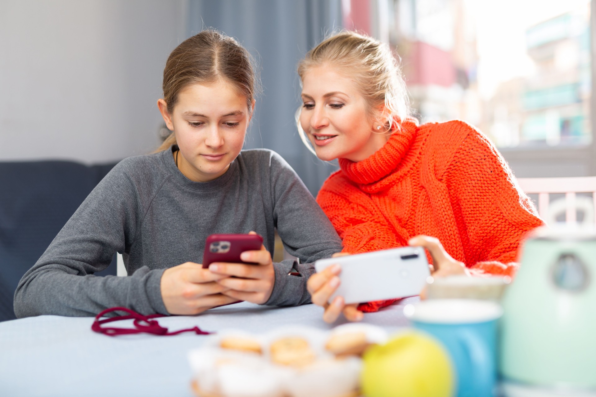 Mother and daughter together playing on their smartphones while sitting at table at home